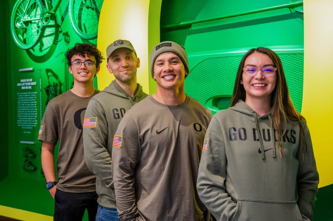 Four students standing in a row and wearing shirts and sweaters from the Nike Duck Veteran collection.