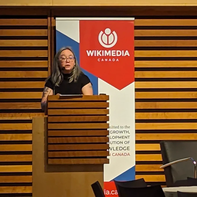 Selena Deckelmann speaks at a podium in front of a Wikimedia Canada banner.