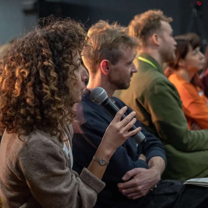 A member of the audiences asks a question, holding a microphone.
