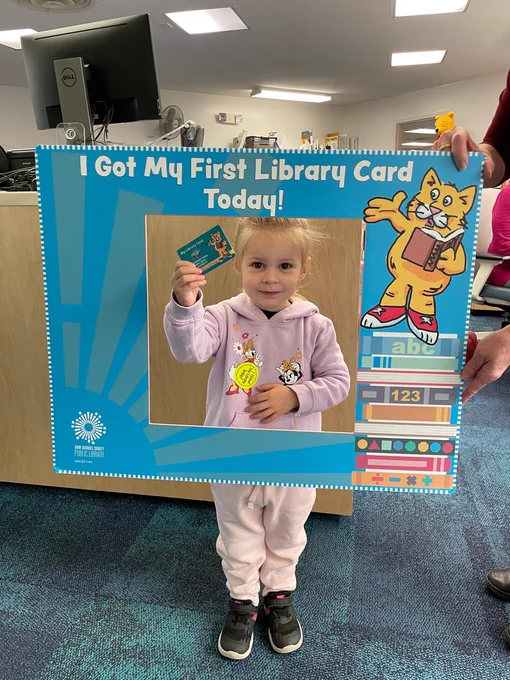 Young child from Broadneck Library holding up their library card with a frame saying, "I got my first library card today!"