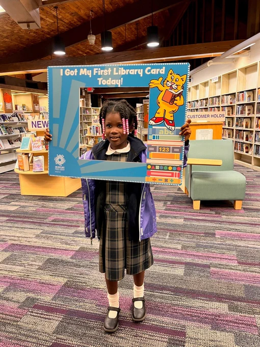 Young library customer holding a sign that reads "I got my first library card today!" at the Brooklyn Park library.