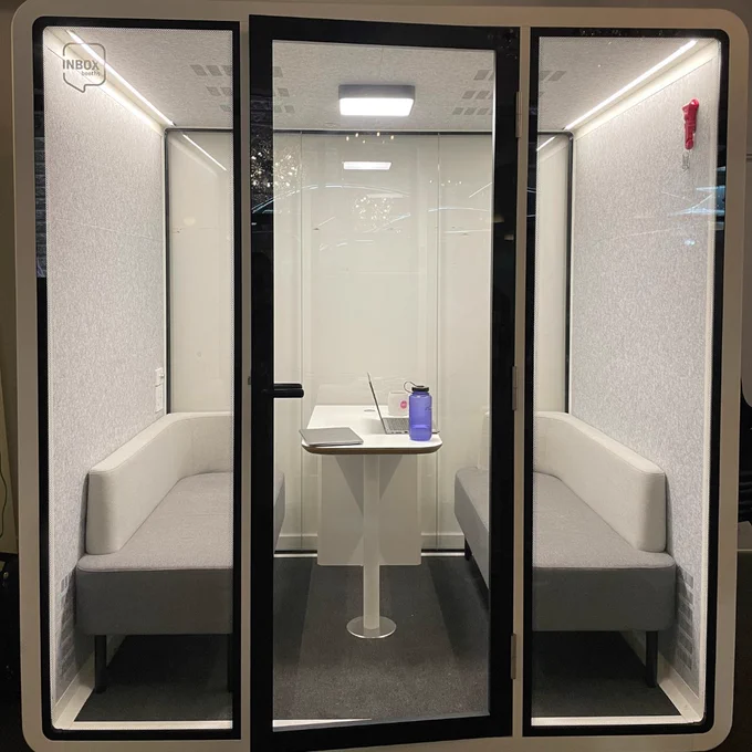 The finalized QUAD meeting room pod, which features two cushioned benches, a table in between, and a light and ventilation system on the ceiling, encased by a tempered glass door. The QUAD is located on CSI Spadina's ground floor.