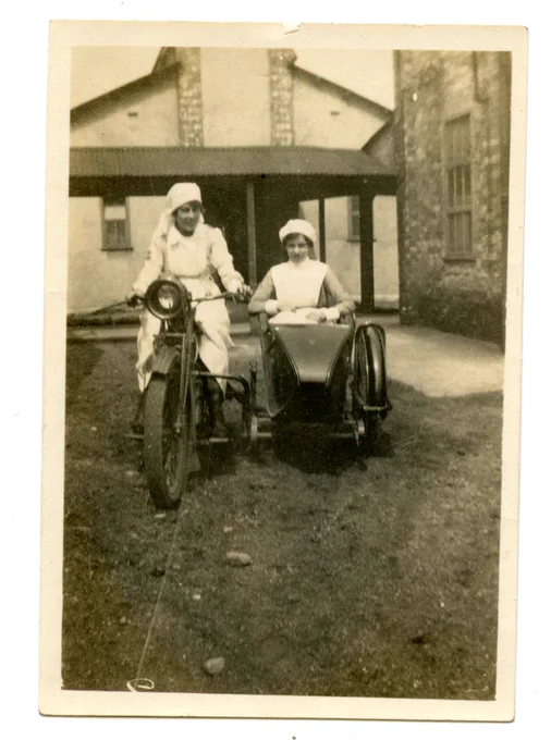black and white image of two red cross volunteer nurses sitting on a motorbike and sidecar