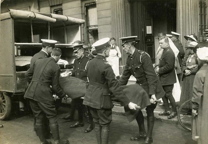 black and white photo of a group of men in army uniform carrying a stretcher with a man on it into an ambulance