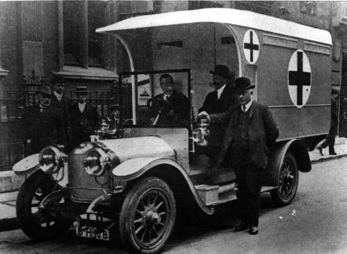 black and white image of three men standing in front of an old Red Cross ambulance