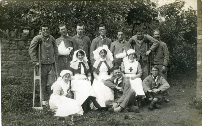 black and white image of four red cross nurses sitting down, and a group of first world war soldiers standing around them smiling at the camera