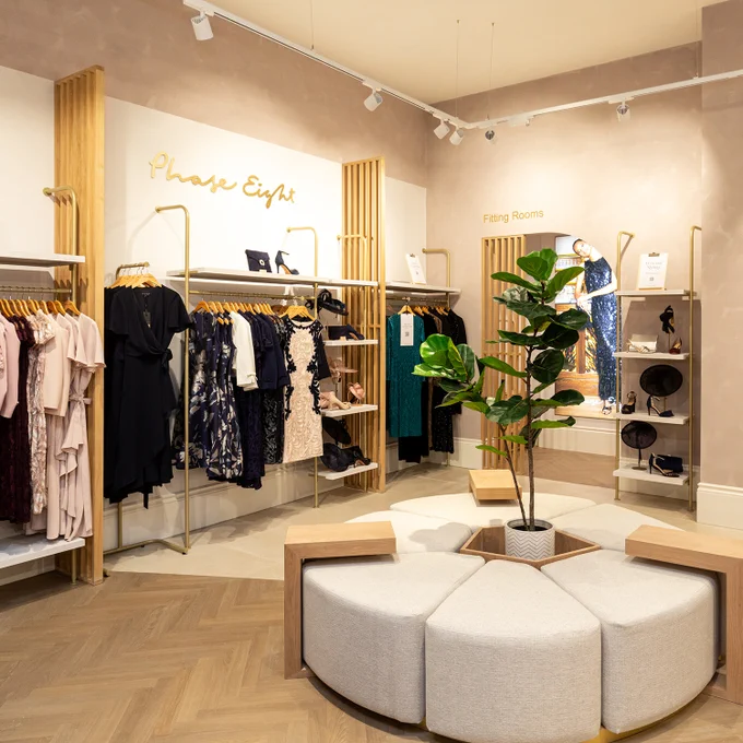 Interior shot of the new Phase Eight store at Merry Hill. A circular seating area with a plant featured in the middle, clothing hanging from wall fittings in the background.