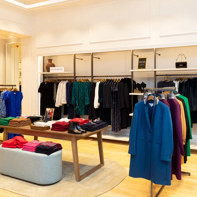 Interior shot of the new Hobbs store at Merry Hill. A wooden table displaying folded jumpers, with wall mounted hanging rails displaying dresses in the background.