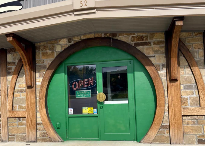 Big green circular door cutout with a brass handle and wooden trim, outside of a stone faced shop.