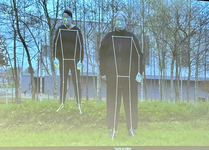 A screenshot of  two women standing in a grassy area. Both wear black. They are facing the camera. Both also have some graphics superimposed on their bodies representing points of image capture on hands, arms, faces, torsos and legs.