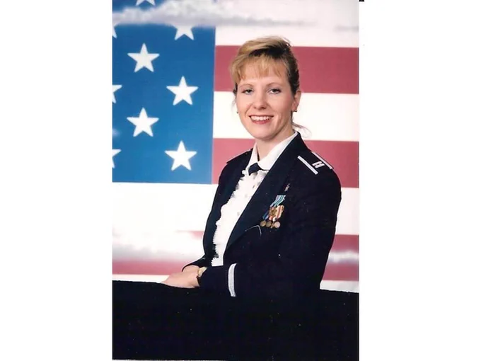 Image of a woman in US military uniform, posing in front of an American flag.