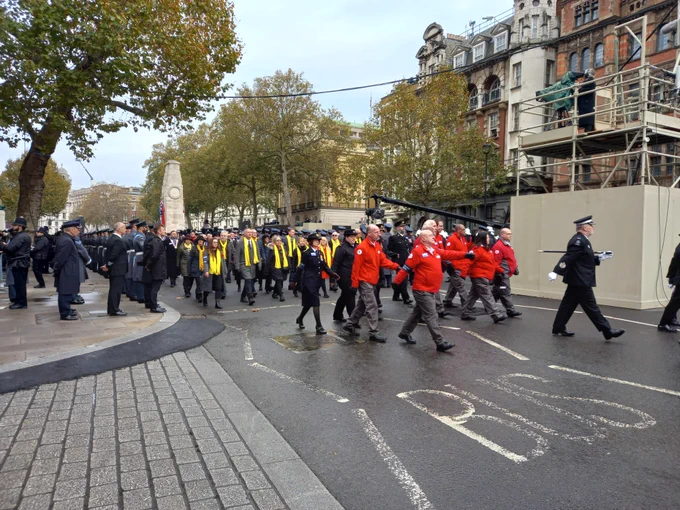 A group of Red Cross volunteers wearing red and grey uniform they are marching with other groups at the Cenotaph in London.