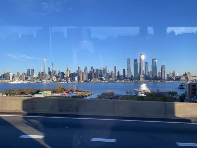 Photo of the NYC skyline through a bus window. The sky is blue & clear and the sun is reflecting off some of the skyscrapers.