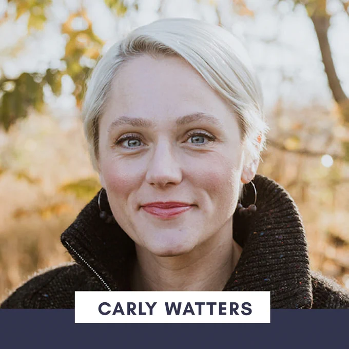 Headshot of Carly Watters, a woman standing outdoors in a knit sweater who has short blonde hair and blue eyes. She is smiling with a closed mouth and is wearing hoop earrings decorated with beads.