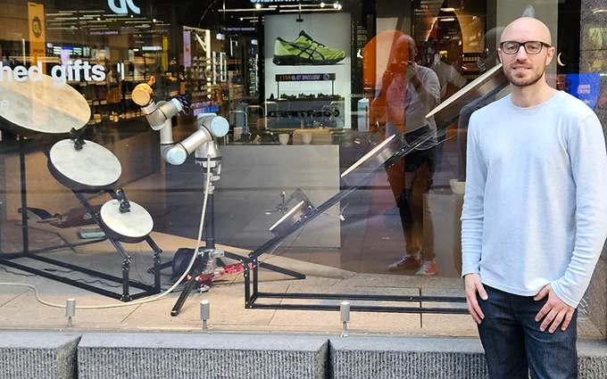 Dr Fred Sukkar (right) is developing algorithms to enable natural and safe human-robot collaborative environments in the manufacturing industry at the Australian Cobotics Centre (ACC). Pictured at the centre of the musical ensemble is a collaborative robot (cobot) holding a caxixi, flanked by six mechanised drums.

