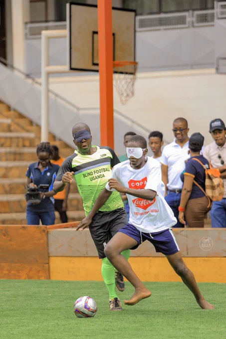 Two blind football players in lemon green and white shirt with dark blue short in pursuit of a ball.