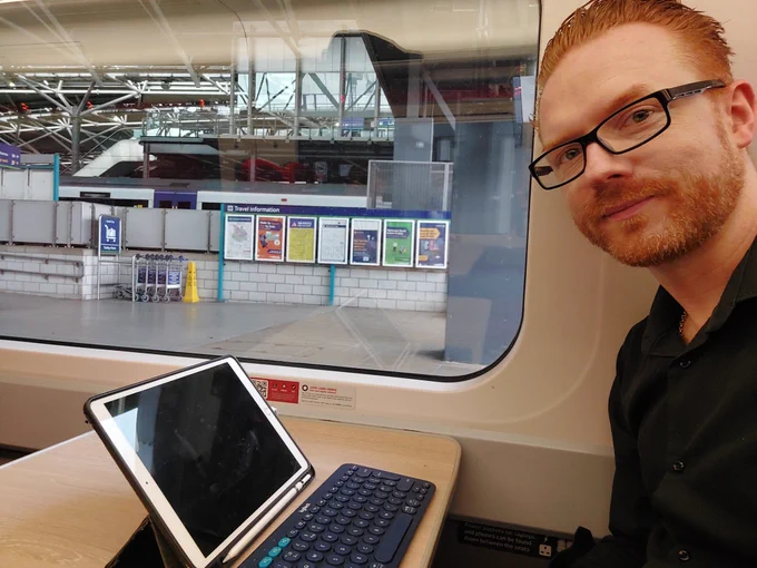 Sat on train with iPad. There is a window showing Leeds Station.