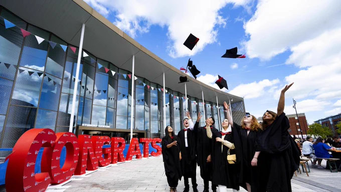 Graduates throwing their hats in the air next to a congrats sign