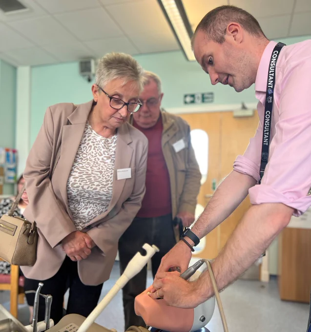 Two members of the public peer over a University staff member who is demonstrating how students use a model head and mouth in their dentistry studies