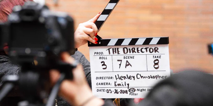 A director holding up a classic film clapperboard on a film set in front of a camera. 