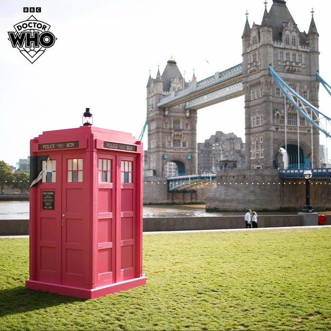 Pink Doctor Who TARDIS, standing in front of Tower Bridge, London.