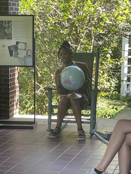 Tiara, a Black woman, holds a globe on her lap as she talks to children seated in front of her.