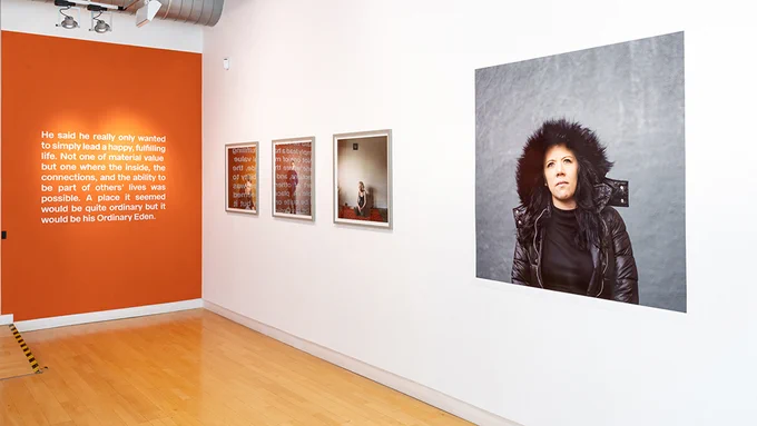 A gallery with an orange wall, white text printed onto it and a white wall will four large framed photographs. 