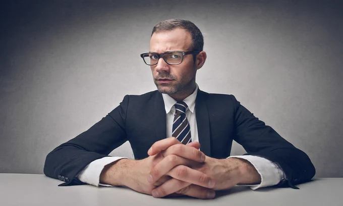 Man in a suit with hands towards the camera and fingers intertwined
