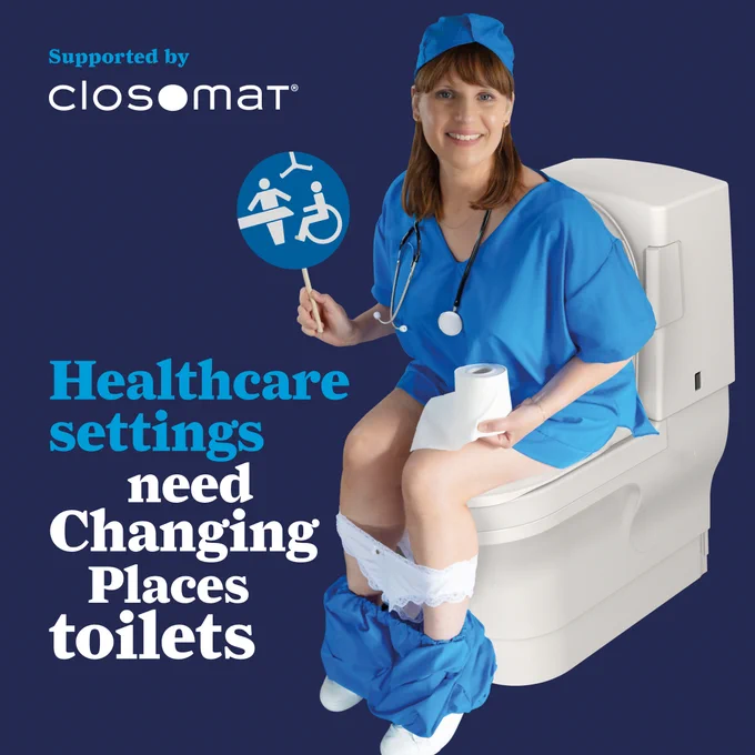 Female sitting on Closomat Wash & Dry toilet wearing scrubs,  white pants & blue trousers around her ankles, holding a Changing Places sign. Text: Healthcare settings need Changing Places toilets.