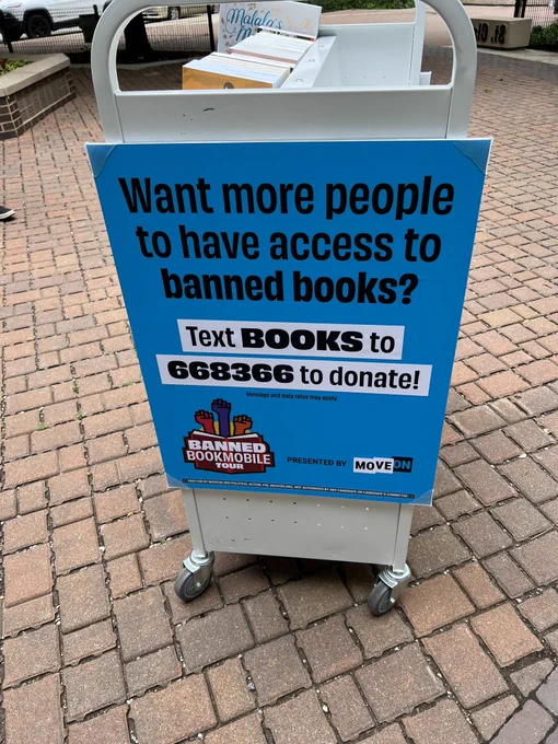 A sign reading "Want more people to have access to banned books? Text BOOKS to 668366 to donate!"
