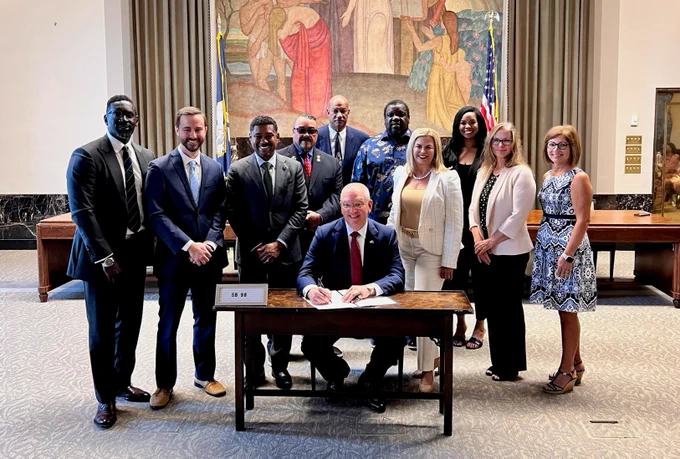 Louisiana legislators, Ochsner Dr. Clark Alsfeld and others stand around Gov. John Bel Edwards as he ceremoniously signs a bill that will allow people to register to be a bone marrow donor when they renew their license