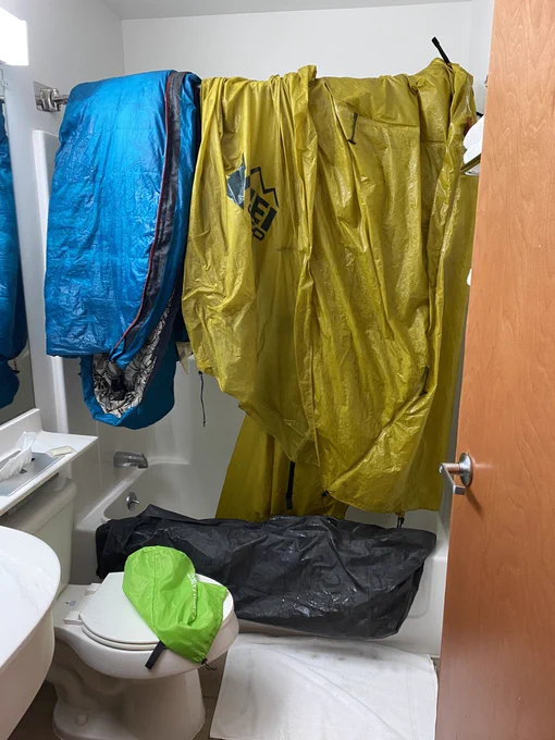 Sleeping bag and rain fly hang to dry in a hotel bathroom. They are visibly soaked.