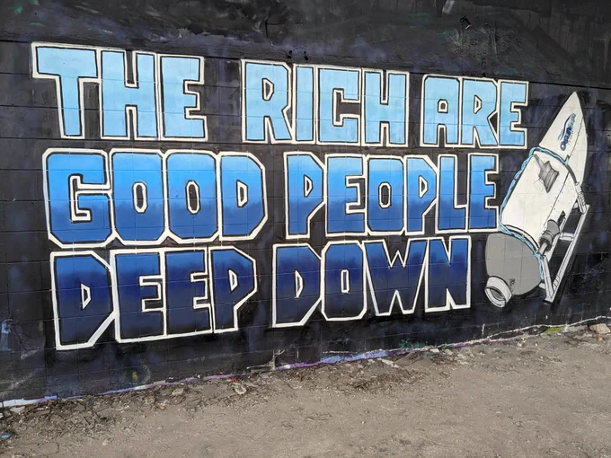 Mural on a black wall featuring the titan submersible and the words "The rich are good people deep down" in blue