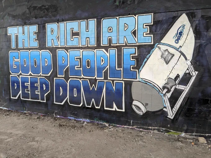 Mural on a black wall featuring the titan submersible and the words "The rich are good people deep down" in blue