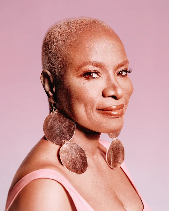 A portrait of Angélique Kidjo, with close-cropped, dyed blonde hair and long, plate earrings.