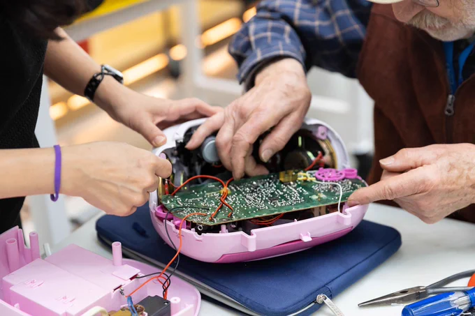 Two people work on a pink radio