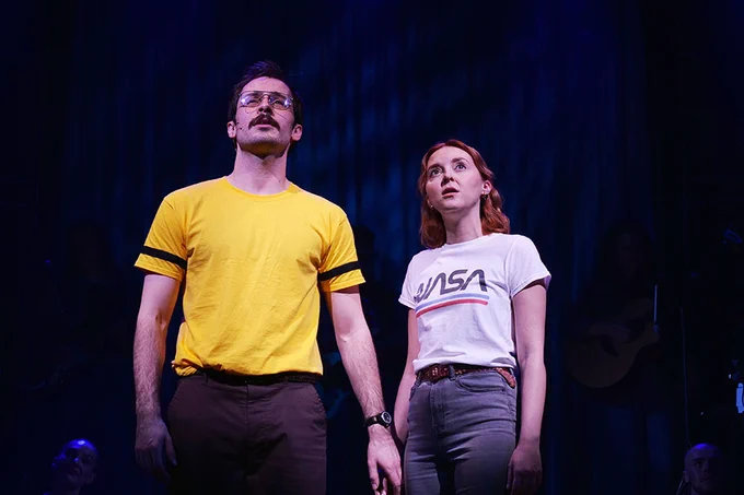 A photo showing two people in tee shirts staring out into the middle distance while on stage