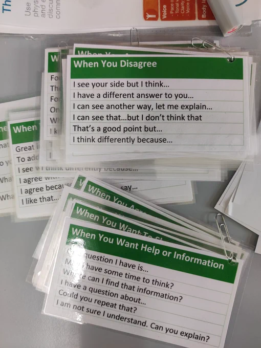 Photograph of small laminated cards with prompts ("When you disagree", "When you want help or information"). Under the prompts, there are sentence stems offering a suggested way to move forward.