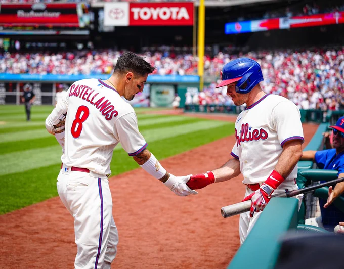 Photo of Nick Castellanos shaking J.T. Realmuto's hand after hitting a home run. They are both wearing the white Phillies uniform and Realmuto has on a blue and red helmet.