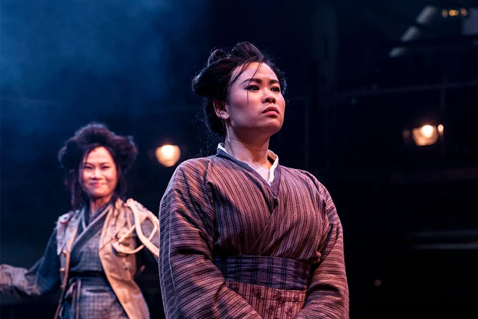 A photo showing two performers on stage in period dress, looking into the middle distance