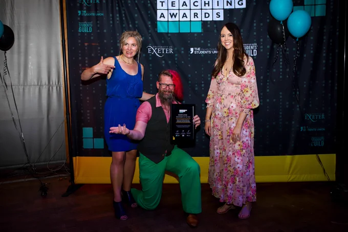 3 members of staff in front of Teaching Awards backdrop. One member of staff is holding an certificate and award.