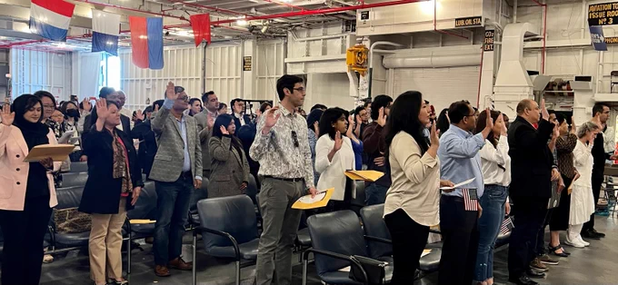 A group of new U.S. citizens raise their right hands to pledge their Oath of Allegiance at the USS Hornet Museum.