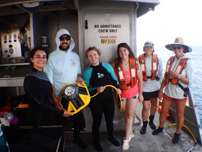 Sanctuary staff wearing dive gear or life vests hold the yellow SoFar buoy and cable as they stand on the deck of R/V MANTA.