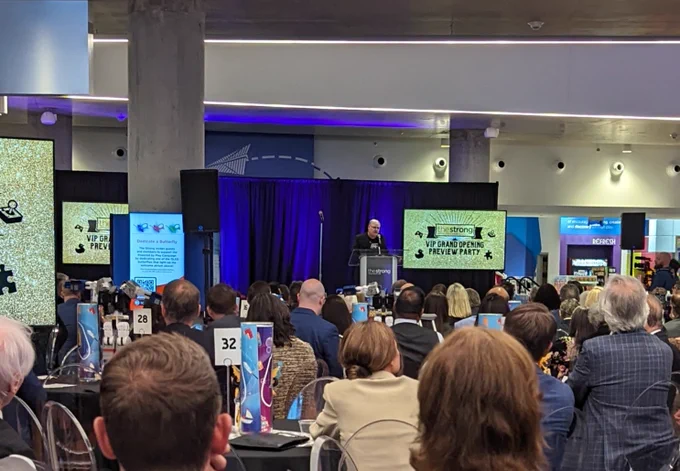 Don James, executive vice president of operations at Nintendo, on stage in front of a seated crowd. To his left is a monitor displaying “the Strong VIP Grand Opening Preview Party”.