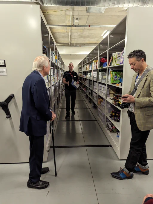 Andrew Borman of the Strong standing between a set of rolling archival shelves. At the end of the stacks to the left is Tom Kalinske and to the right stands Peter 