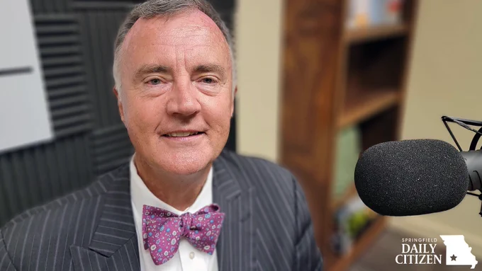 Brian Fogle, wearing a bow tie of course, sits next to a microphone