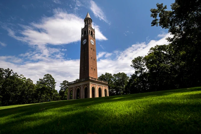 The Bell Tower on the campus of UNC Chapel Hill against a green field with bright blue skies.