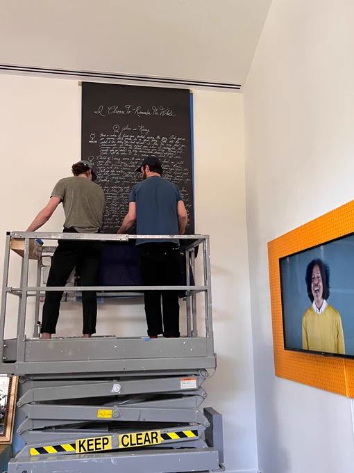 Two men on lift install a chalk board on wall