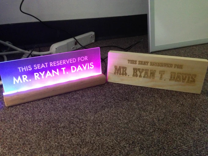 The light up sign from the previous picture next to a wooden cutout in a western serif font that also reads "This seat reserved for Mr. Ryan T. Davis"