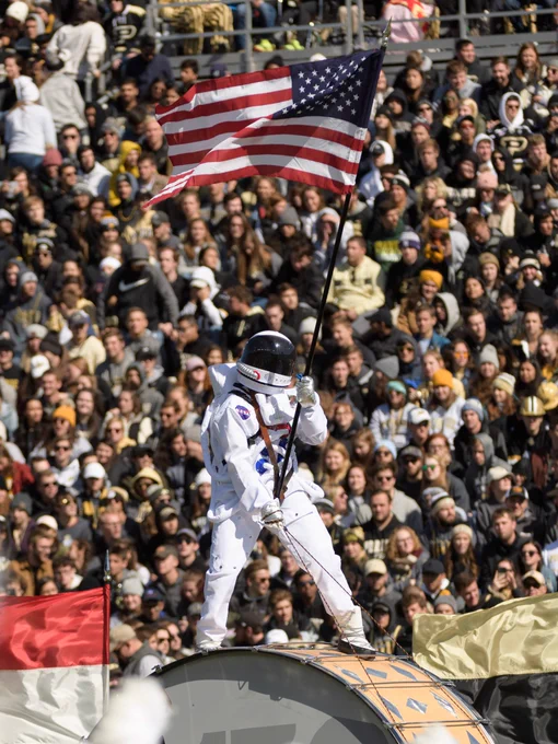 A person wearing a NASA space suit holds an American flag while standing on top of The World’s Largest Drum™.